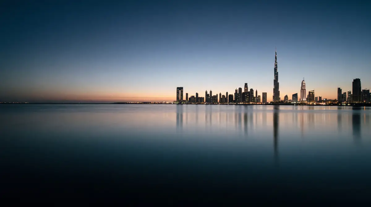 La silhouette de Dubaï et le Burj Khalifa au-dessus d'une eau calme, juste après le coucher du soleil